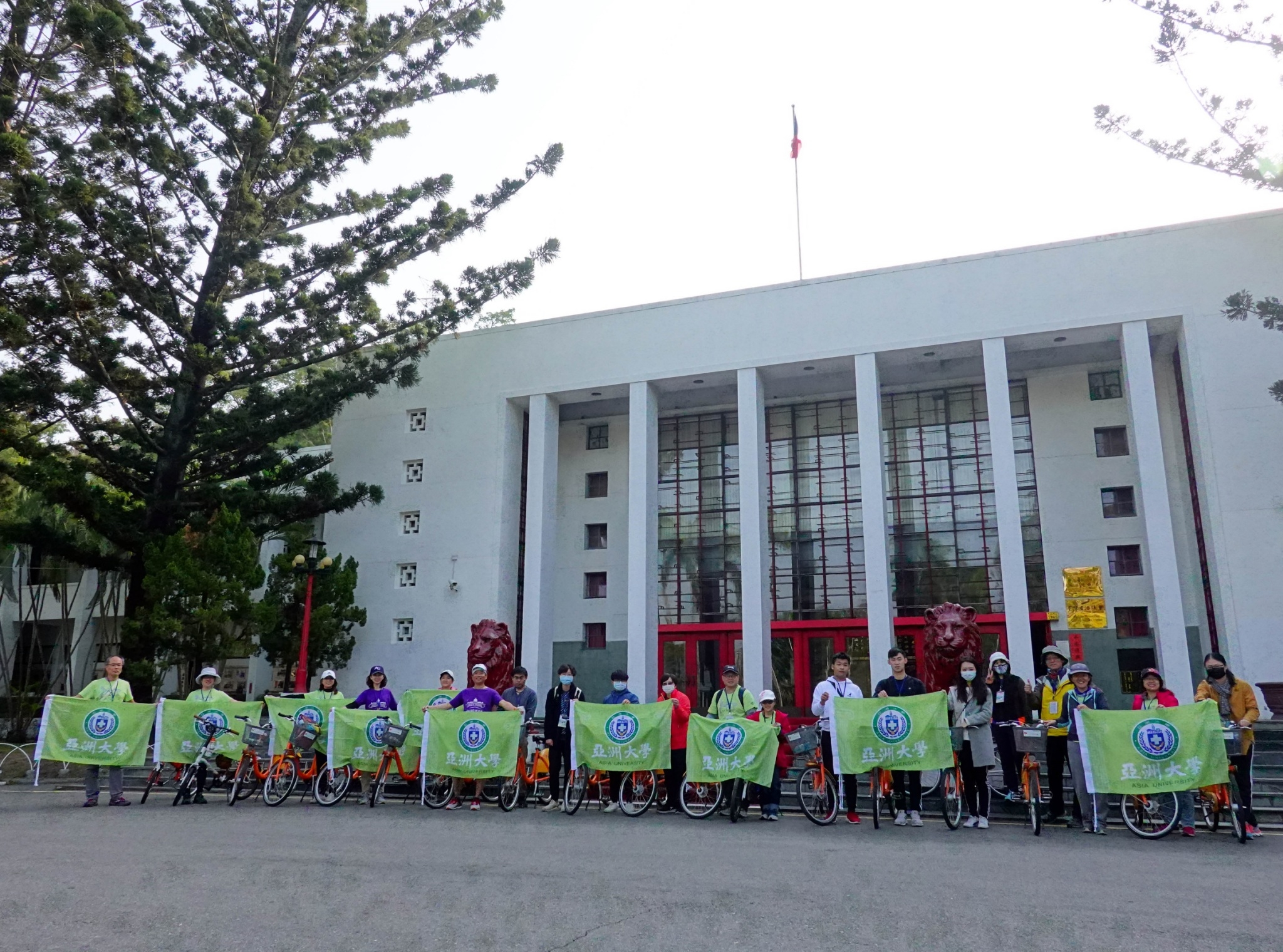 亞大主任秘書施能義(左6)與繞騎霧峰20K團隊成員拉開校旗,歡慶亞大20週年活動。