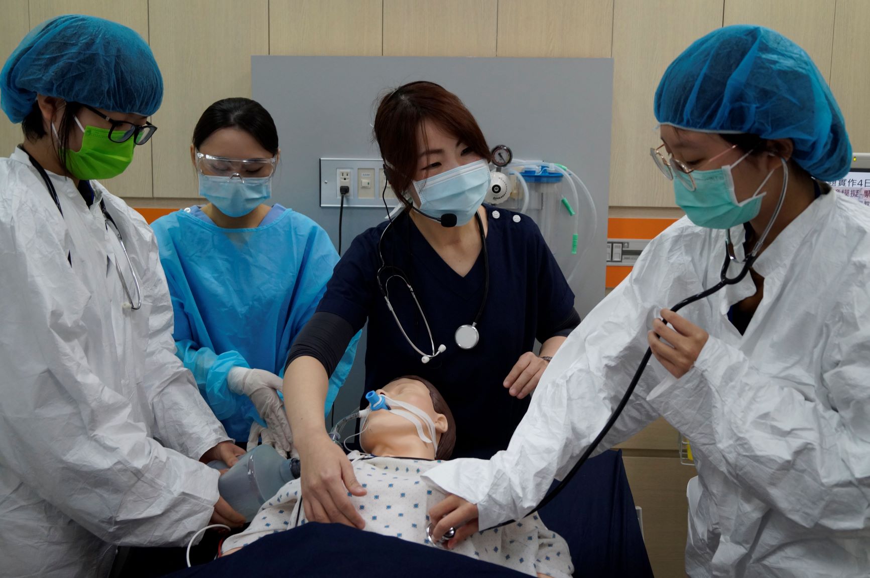亞大護理學系彭逸稘老師(中),利用智慧高階模擬人,設定緊急救護擬真情境,讓學員們(左、右戴藍色帽子者)體驗。