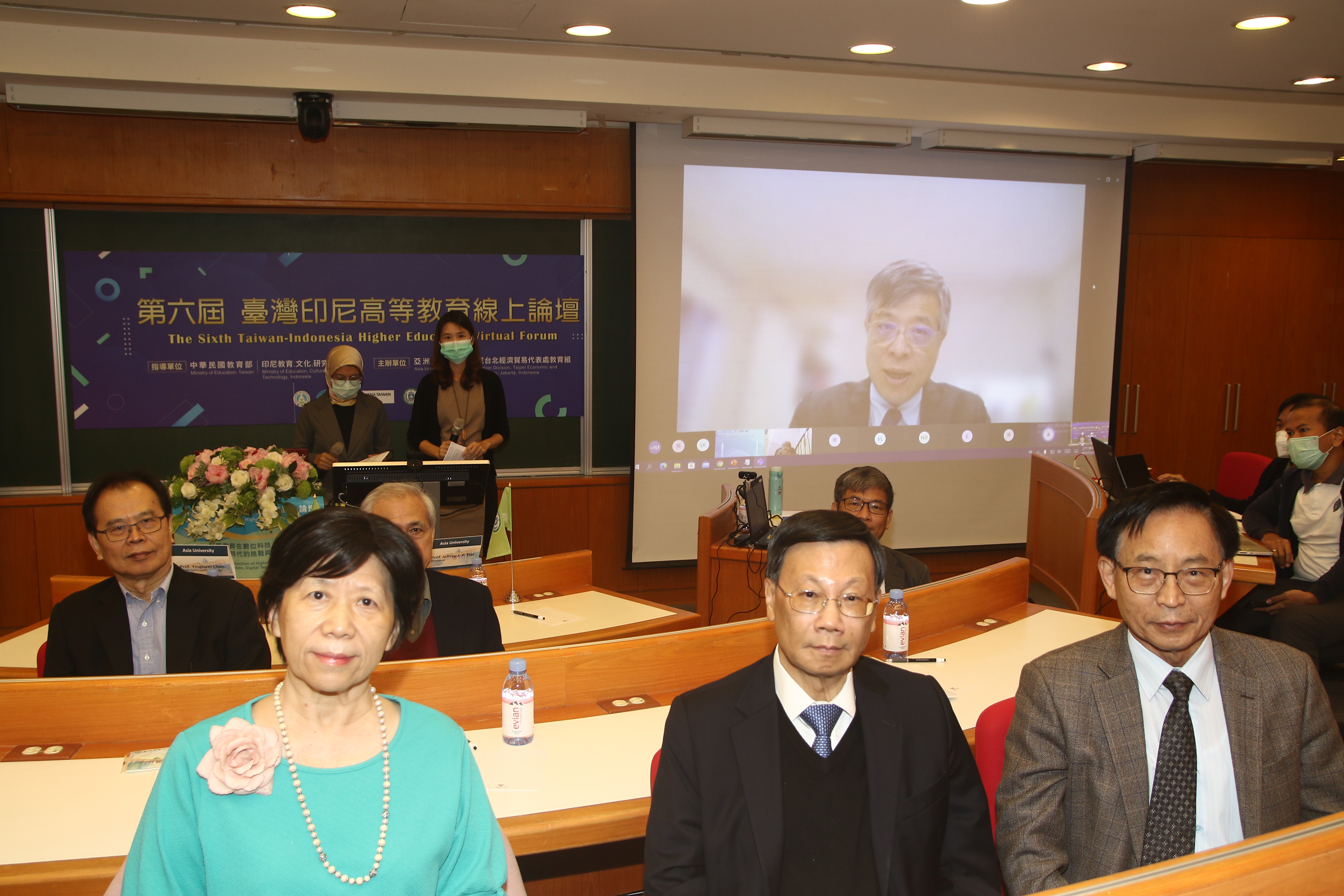 教育部次長劉孟奇(後方大螢幕)視訊致詞,亞大校長蔡進發(前排中)、副校長柯慧貞(前排左)、國際學院院長陳英輝(前排右)等與會。