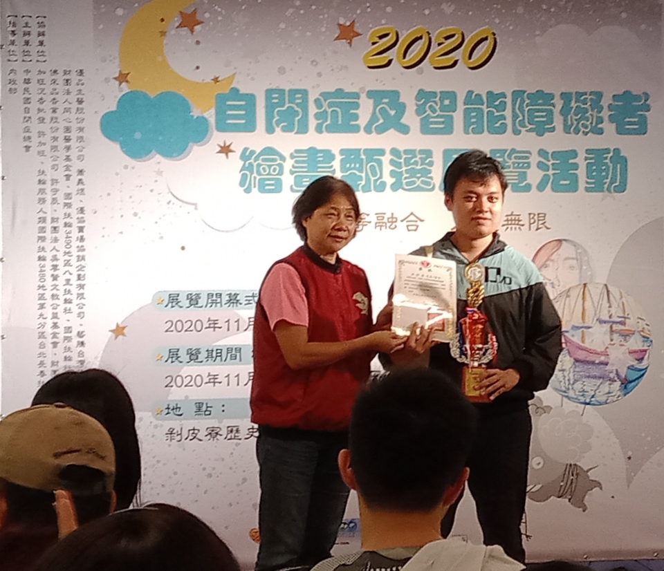 數媒系碩士生洪梓晏(右)以「愛心行動」作品,獲全國性身心障礙繪畫比賽成人組佳作,接受頒獎表揚。
