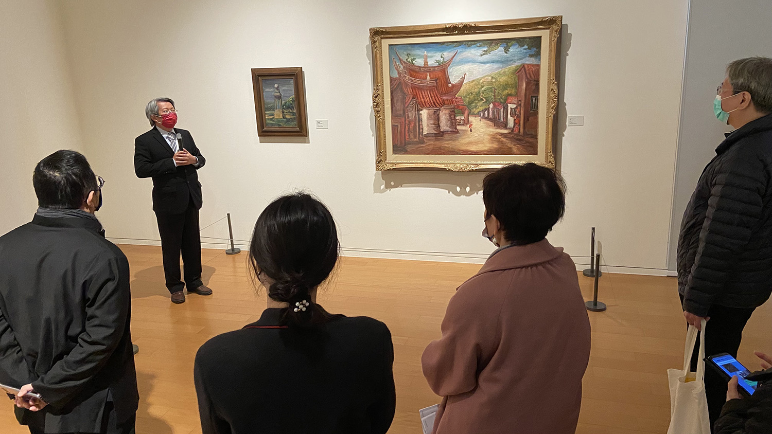 亞美館館長潘襎(左)帶領觀展者,參觀「尋找台灣的色彩-前輩畫家眼中的台灣」展區,圖中兩幅作品都是前輩畫家陳澄波的畫作,右為「古廟」,左為「北迴歸線」