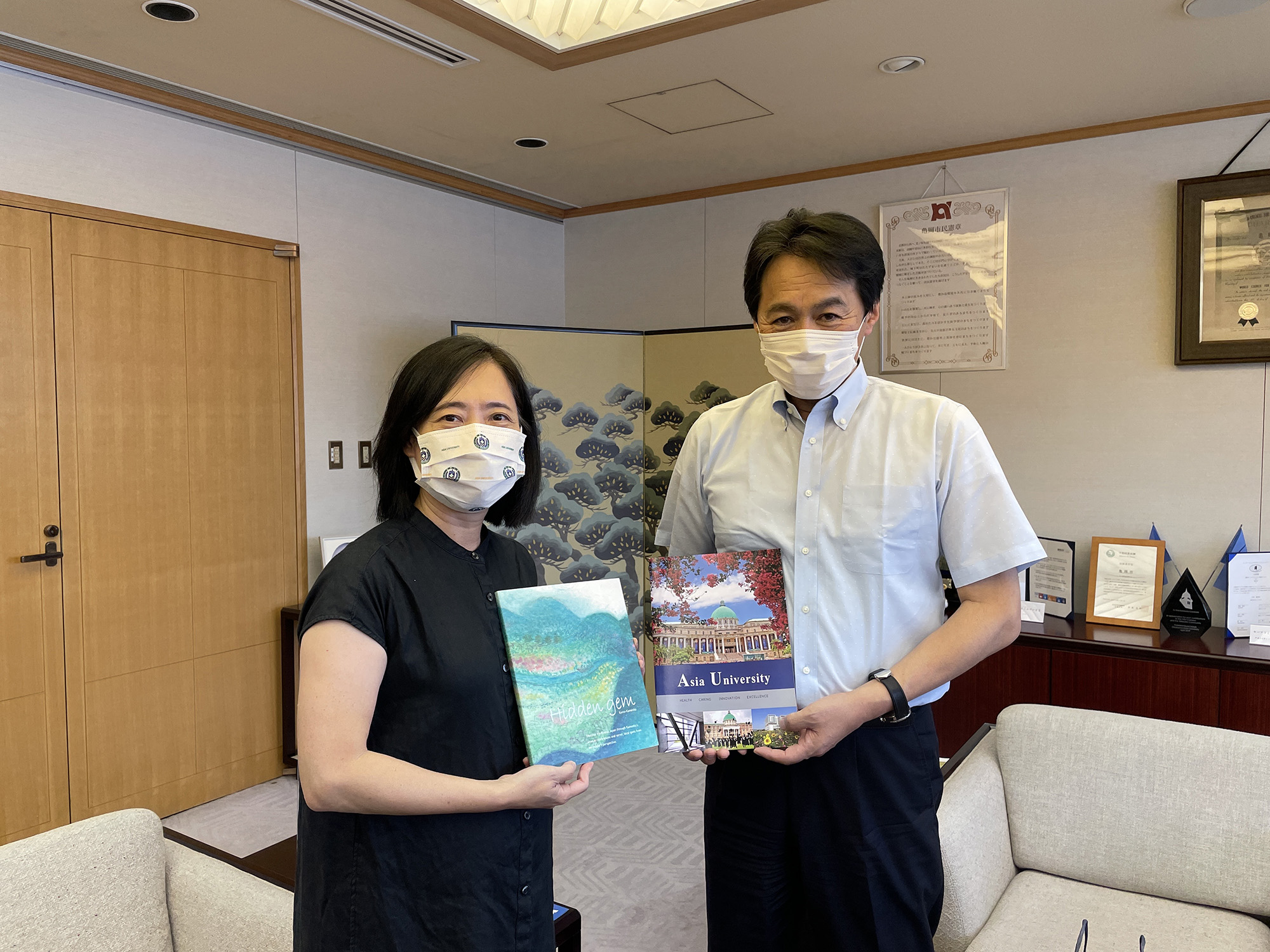 圖為日本京都亀岡市長桂川孝裕(右),和亞大室設系老師林佳慧,交換亀岡市和亞大的介紹資料
