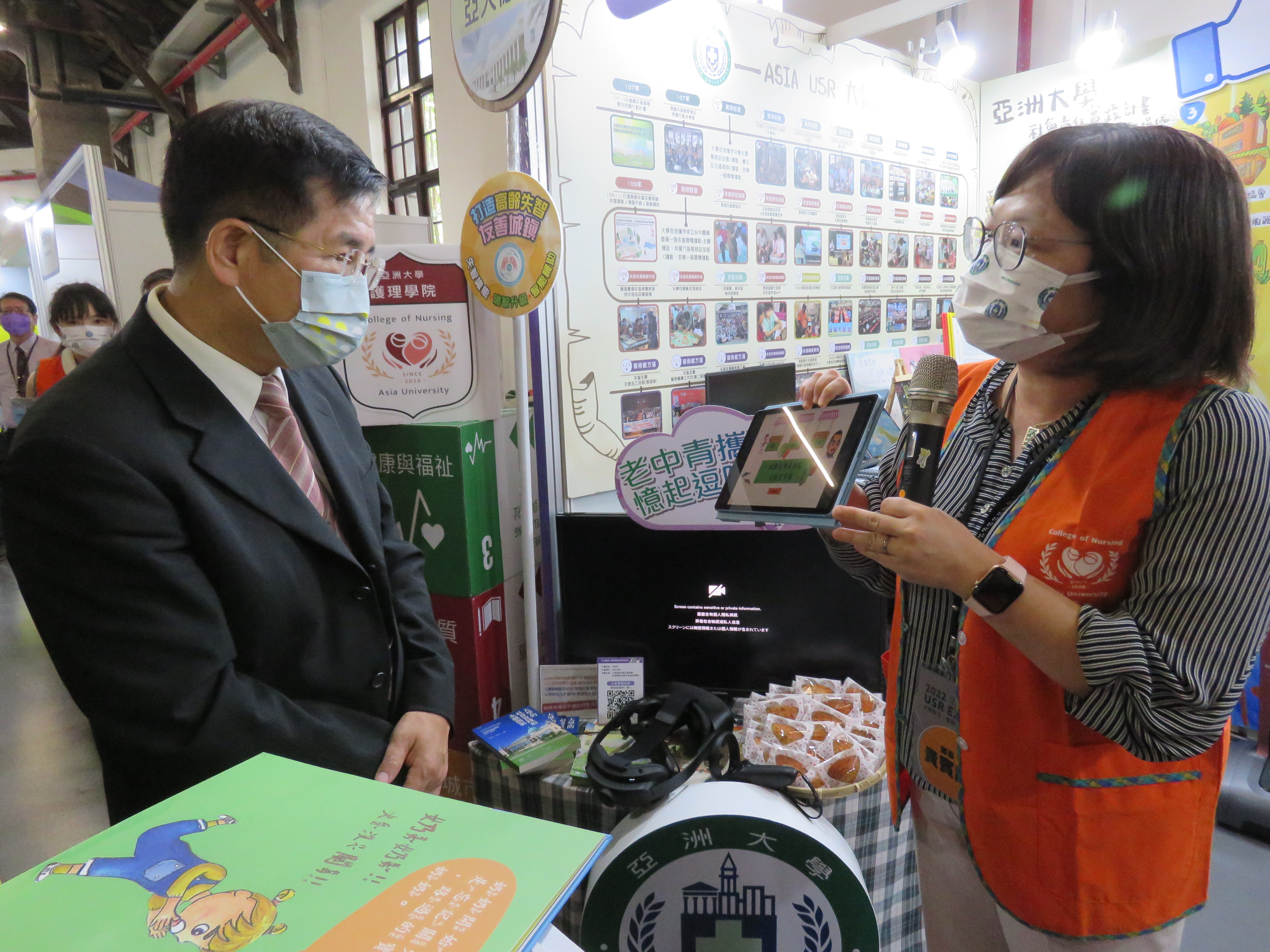 圖為亞大USR計畫主持人、護理學院長吳樺姍(右),向教育部長潘文忠介紹亞大護理學院、資電學院研發的智慧化防失智手遊App功能。