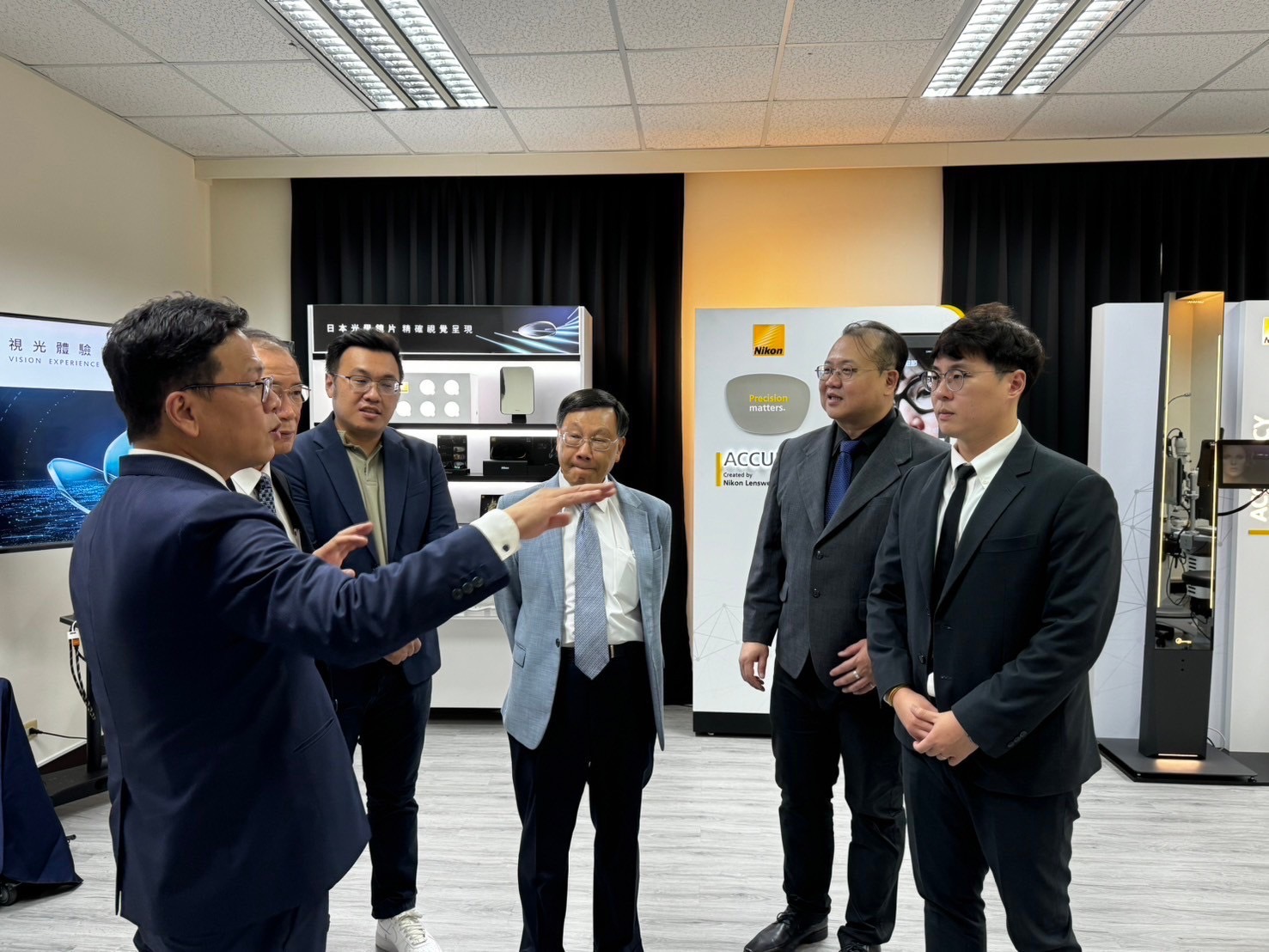 圖為亞大校長蔡進發(中)等,聆聽法商依視路公司徐志成總經理,介紹亞大視光系「Nikno視光體驗中心」的設備。