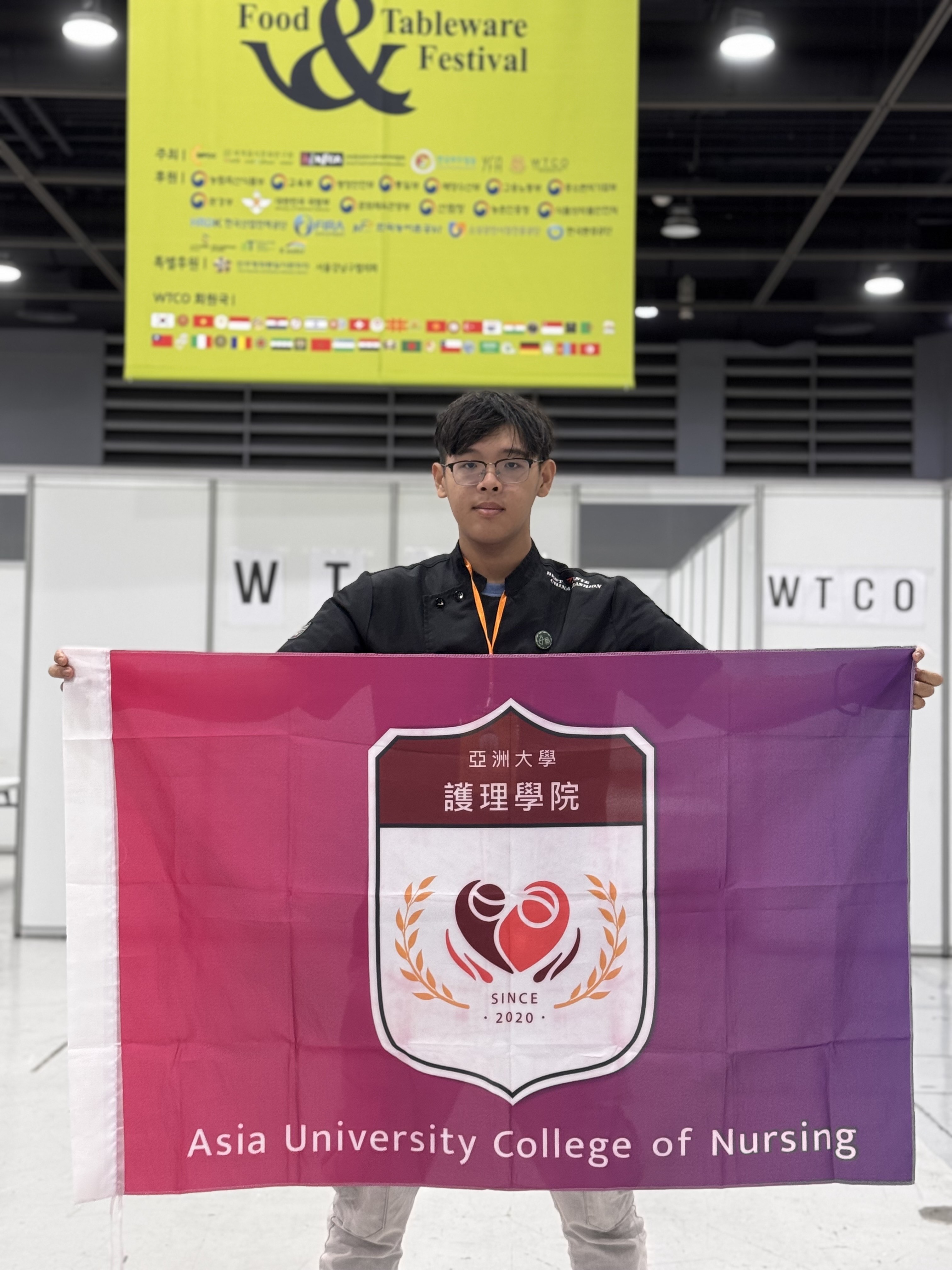 亞大護理系林明宏同學,在韓國首爾aT會展中心高舉護理學院院旗。